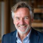 Portret van Hendrik de Vries, oprichter van Kust Timmer, glimlachend voor een houten werkbank.